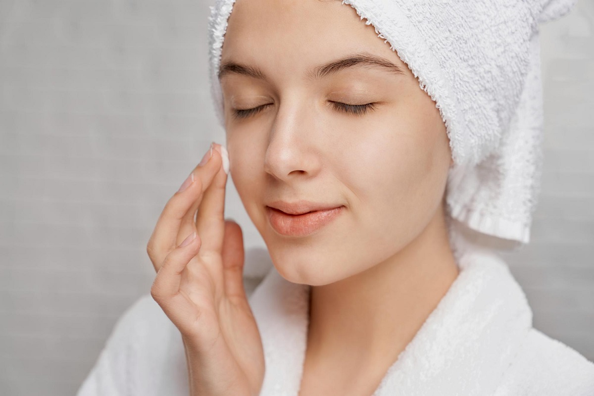 Mulher aplicando creme no rosto, iniciando rotina de skincare para pele saudável e hidratada.