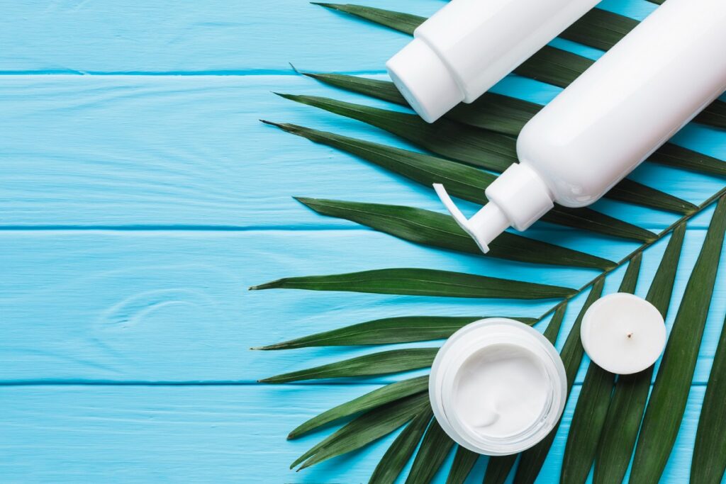 Produtos de skincare com embalagens brancas sobre folhas tropicais e fundo azul claro